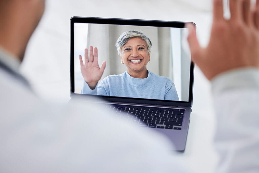 Doctor says hello to his patient during a virtual appointment using his laptop