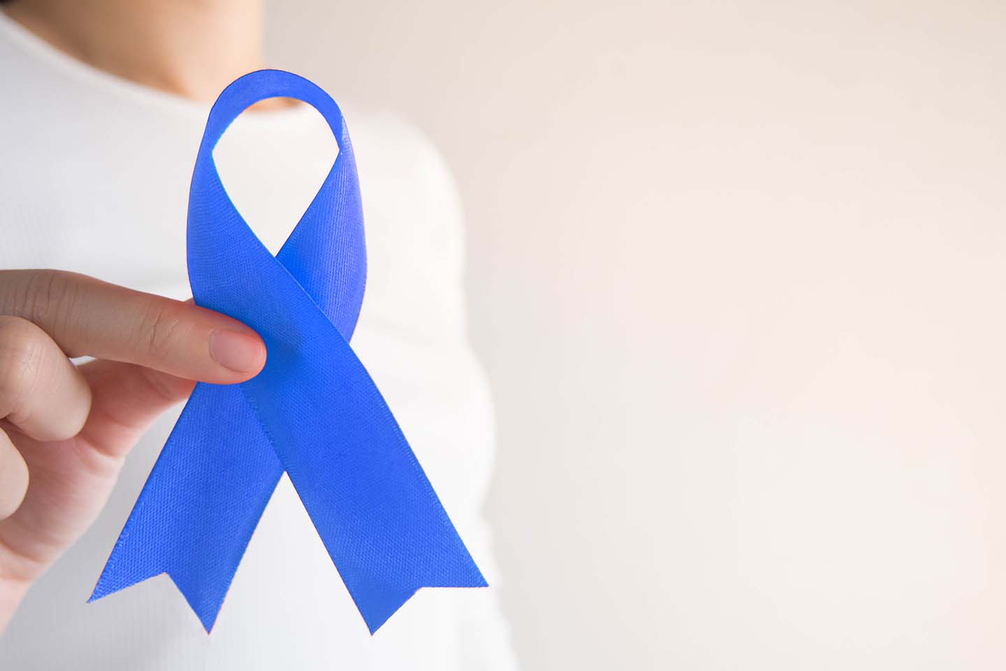 hand holding a blue ribbon showing support for people living with colon or colorectal cancer
