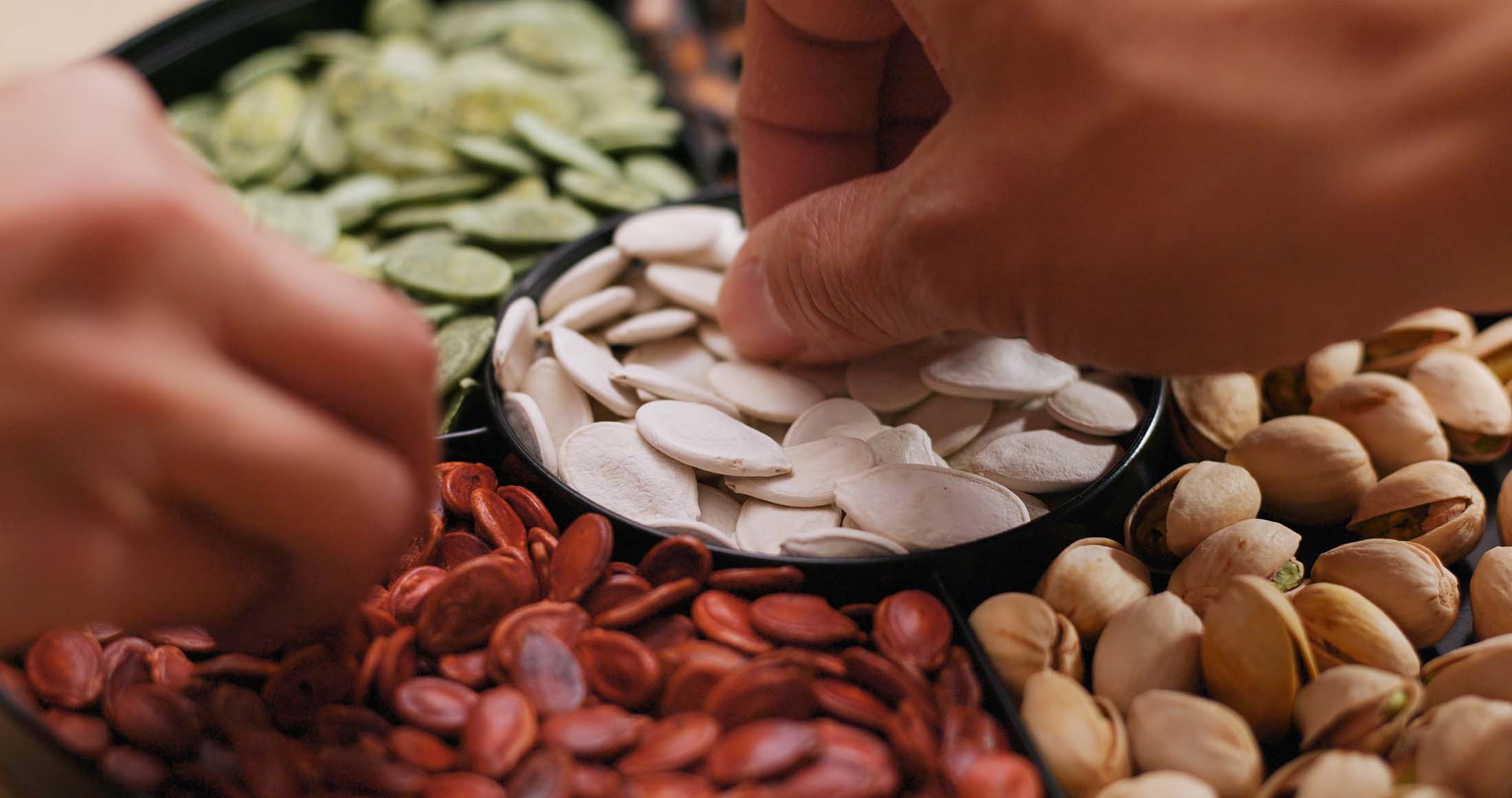 hands reaching for assorted seeds and nuts